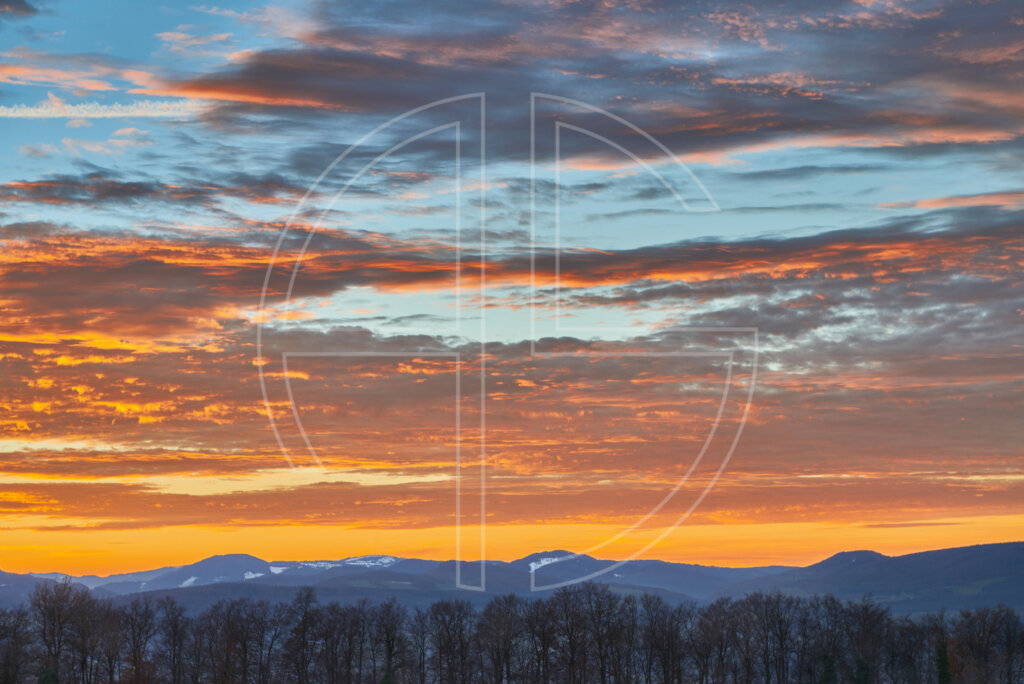 A golden sky at dusk. On the horizon loom hills.