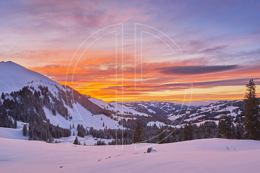 Winter sunset with a golden and orange sky. Snow adorns the mountainous landscape.