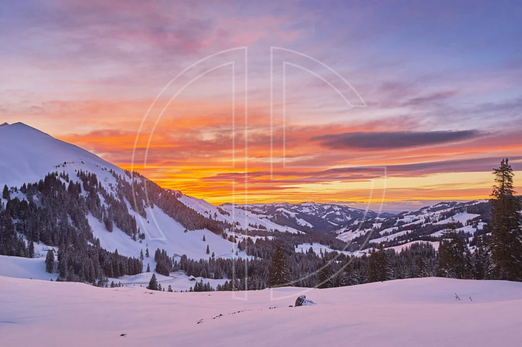 Winter sunset with a golden and orange sky. Snow adorns the mountainous landscape.
