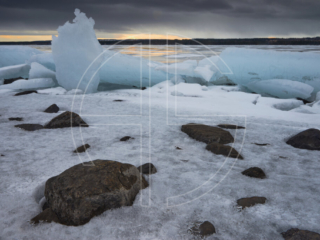 Sunset on a river with lots of ice. The skies brood in shadow.