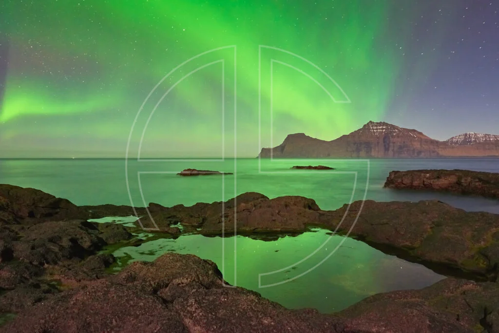 Northern Lights at the sea. The foreground has rocks with water puddles.