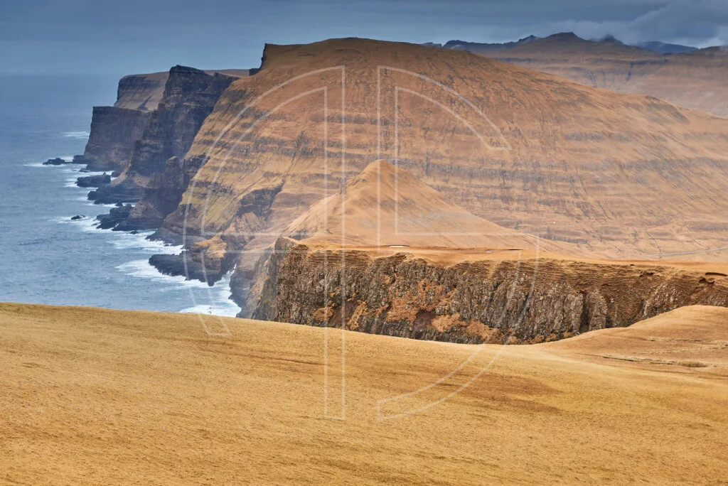 Enormous cliffs from a vantage point. The ground glows in golden brown.