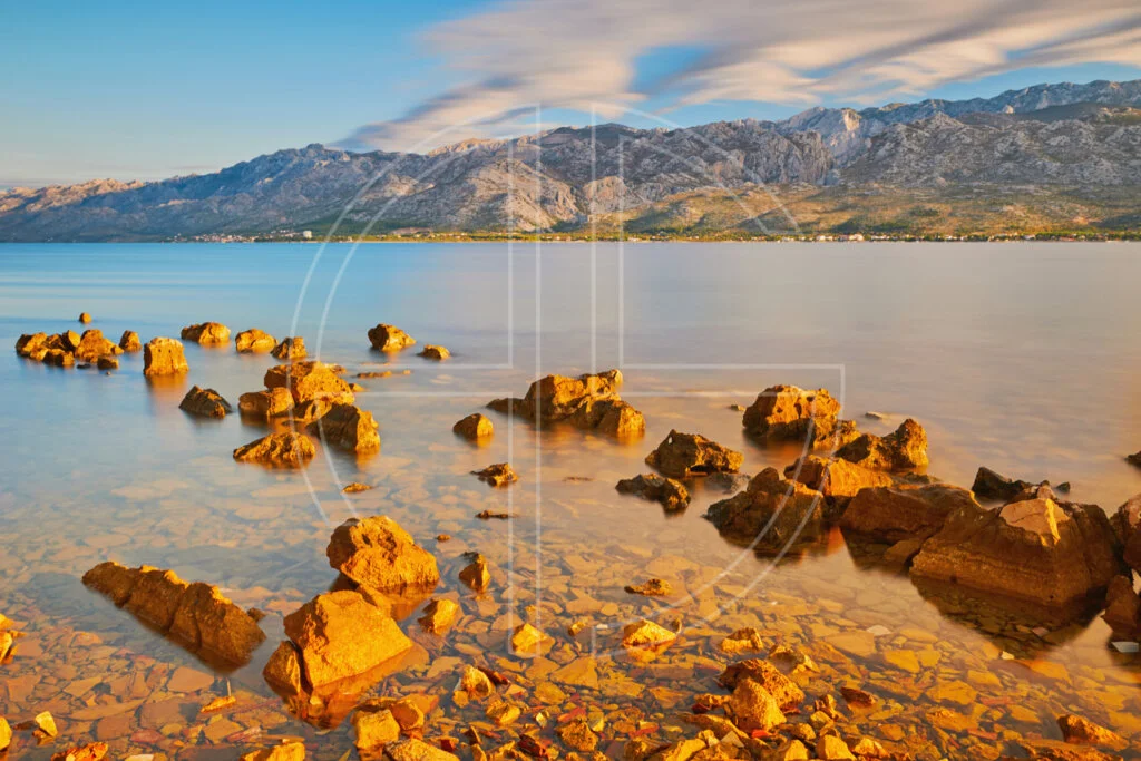Blind At Heart The stones in the foreground bathe in golden light at sunrise by the sea.