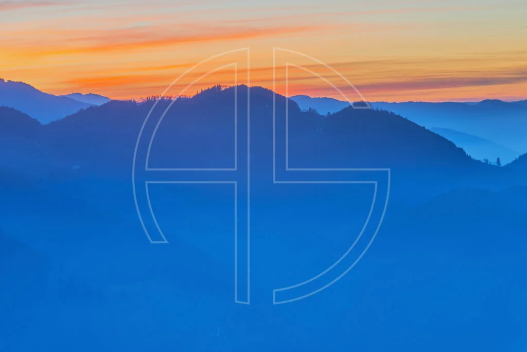 Wooded hills in deep blue. The sky's colour glows in orange.