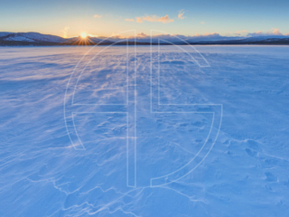 Sunset at a snow-covered frozen over lake.
