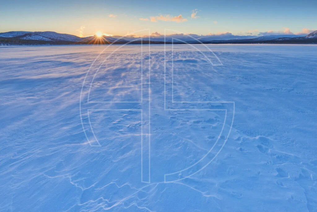 Call Out The Dark Sunset at a snow-covered frozen over lake.