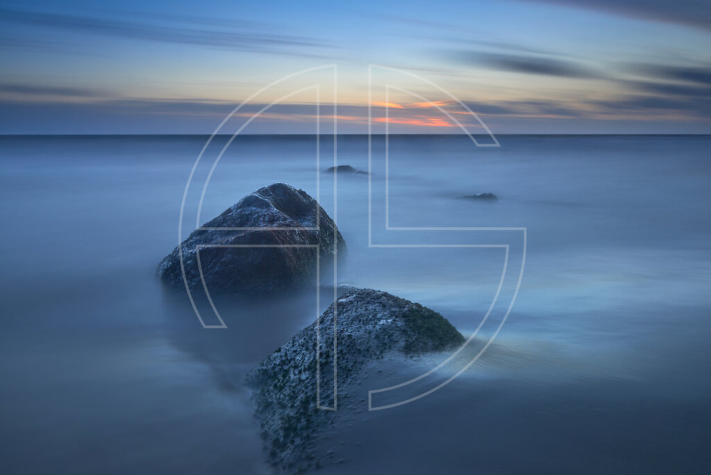 Dusk at the sea. Two large stones grace the foreground.