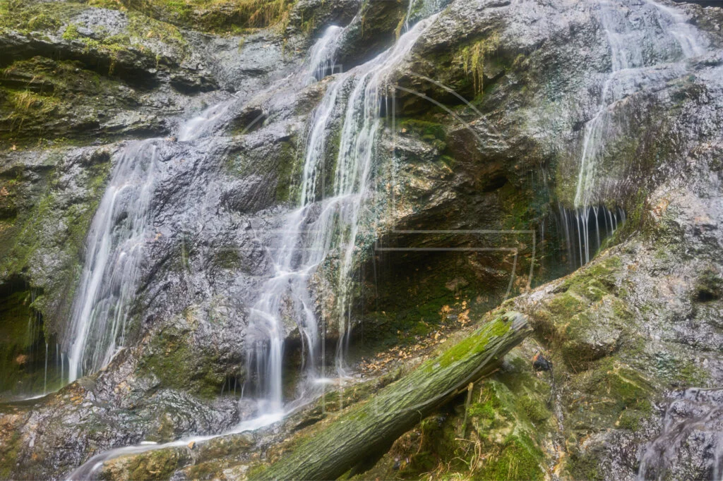 Small waterfalls cascade over rocks with a log in the front.