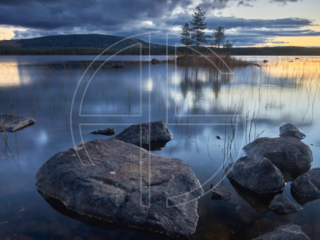 Gloomy Reflections Big stones in the foreground and a lake in the background at sunset.