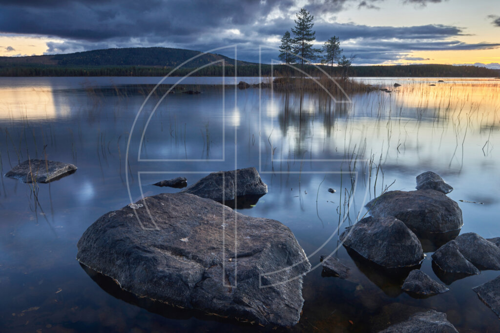 Big stones in the foreground and a lake in the background at sunset.