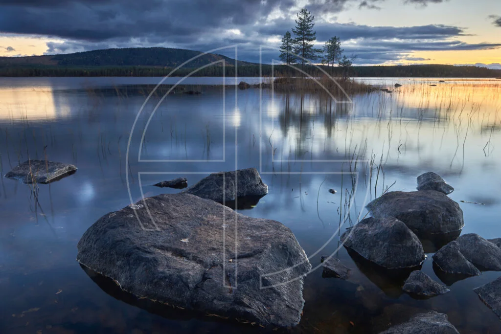 Big stones in the foreground and a lake in the background at sunset.