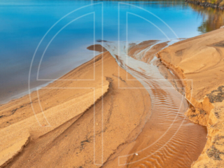 The sun lights the golden sand. A lake lies in the background.