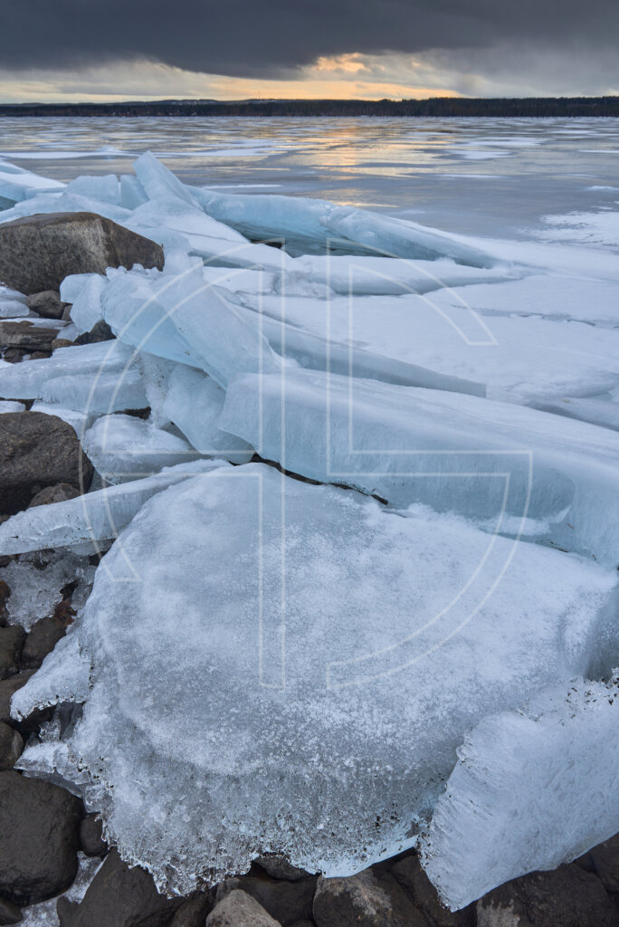 Sunset on a river with big slabs of ice. The skies brood in shadow.