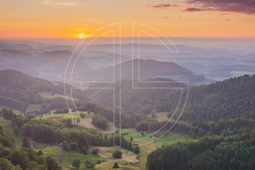 Hazy, orange sunset from a vantage point looking over a hilly landscape.