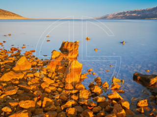 Lost To Apathy The stones in the foreground bathe in golden light at sunrise by the sea.