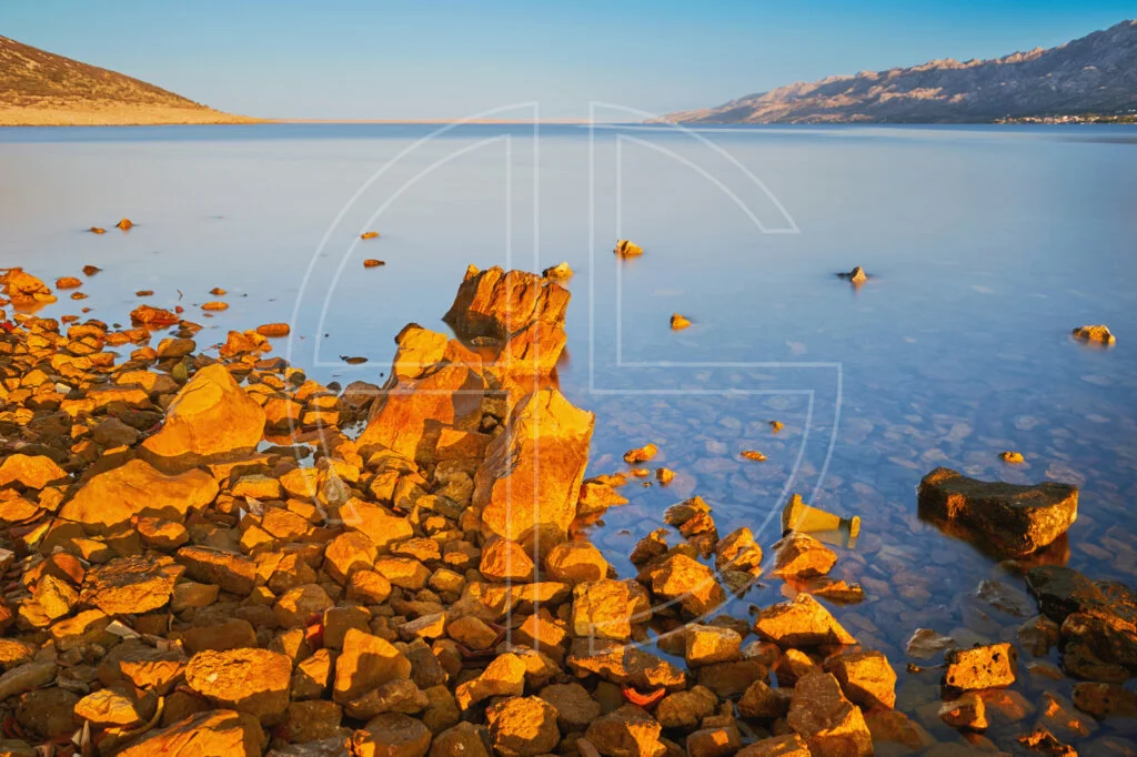 Lost To Apathy The stones in the foreground bathe in golden light at sunrise by the sea.