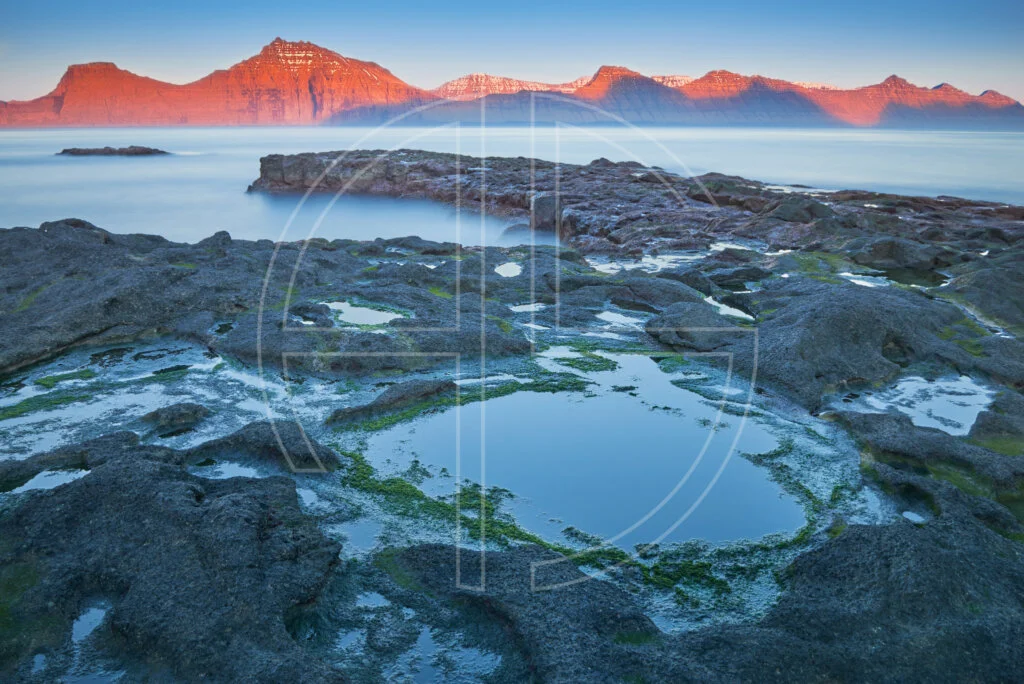 Sunset at the sea. The foreground has rocks with water puddles.