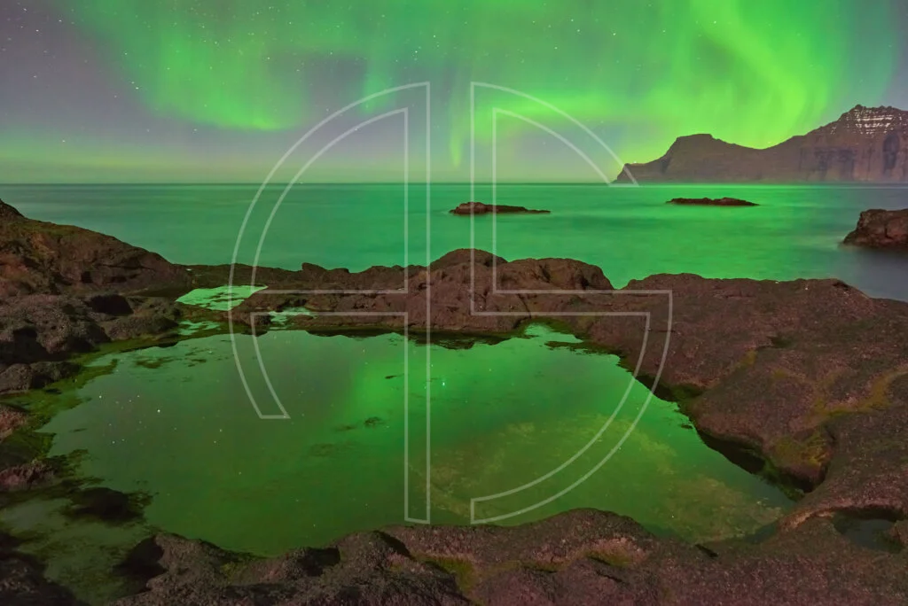 Northern Lights at the sea. The foreground has rocks with water puddles.