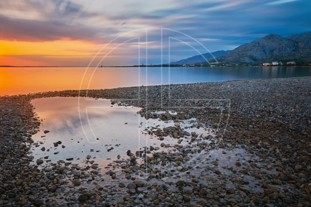 Regain The Fire The sun sets at the sea with stones at the beach.