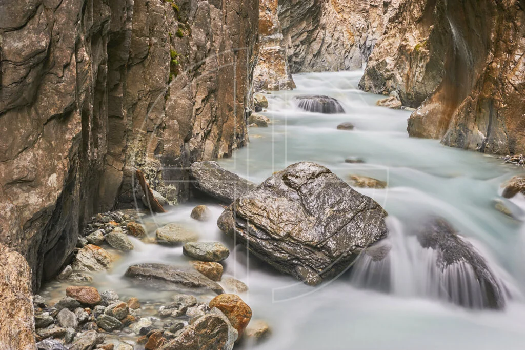 Silky smooth water flows through a glacier gorge. A big stone stands in the foreground.