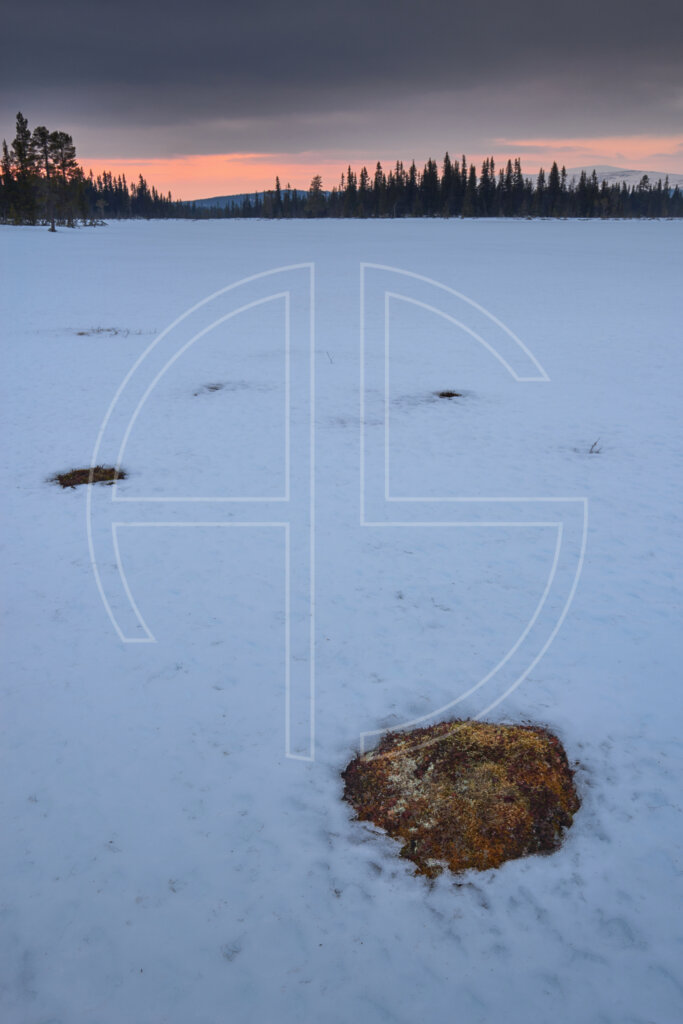 Sunset at a snow-covered lake. The sky holds an overcast colour with a touch of orange.