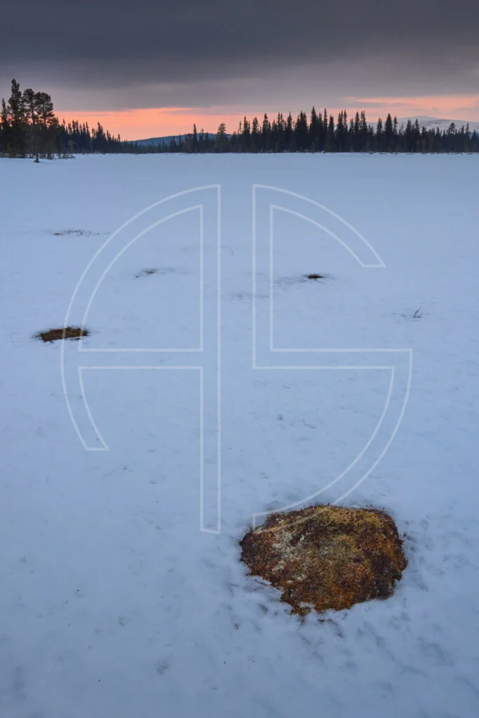 Sunset at a snow-covered lake. The sky holds an overcast colour with a touch of orange.