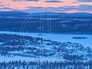 From a vantage point in winter's dusk, a small village sprawls below. The sky blushes with a pink colour.