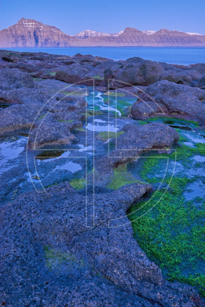 Blue hour at the sea. The foreground has rocks with water puddles.