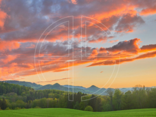 Green hills at sunset. The vast sky has orange clouds.