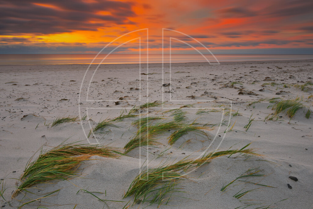 Sunrise at a sand beach, with the sky glowing in deep orange and gold.